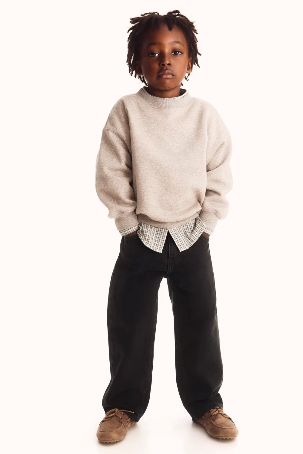 Child in a beige sweatshirt, checked shirt and dark jeans